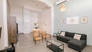 Una sala de estar moderna con un sofá gris, una mesa de centro de vidrio, sillas de mimbre y un comedor con mesa y sillas.