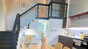 Una cocina moderna con comedor, que incluye una mesa de madera y sillas de mimbre, una escalera y una isla de cocina con electrodomésticos.