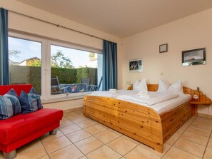 A bedroom with a wooden bed, a red sofa, a large window, and a view of the outside. - Apartment 'Direkt Am See' with Lake View, Private Terrace and Wi-Fi (Malchow)