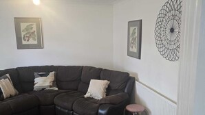 Una sala de estar con un sofá de cuero marrón oscuro, dos impresiones enmarcadas de motivos botánicos, un adorno metálico en la pared y una mesa de centro de vidrio.