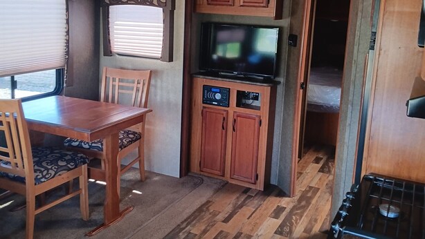 Un intérieur de camping-car compact comprenant un coin repas, une kitchenette et un téléviseur.