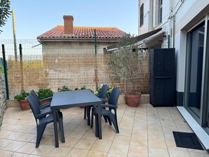 Eine Außenpatio mit Tisch, Stühlen, Topfpflanzen und einem Gebäude im Hintergrund.