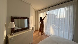 Een hotelkamer met een groot bed, een kaptafel, een spiegel en een raam met dunne gordijnen.