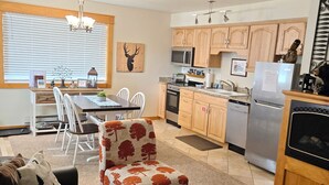 A modern kitchen with wooden cabinets, a microwave, and a refrigerator. There is a dining area with a table and chairs, and a ceiling fan above. - Elk Meadow Condo #6047 (Estes Park)
