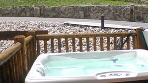 A hot tub with a wooden deck and stone wall in the background. - Elk Meadow Condo #6047 (Estes Park)