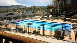 A private pool area with a wooden deck, a fenced swimming pool, and a building with a balcony. - Elk Meadow Condo #6047 (Estes Park)