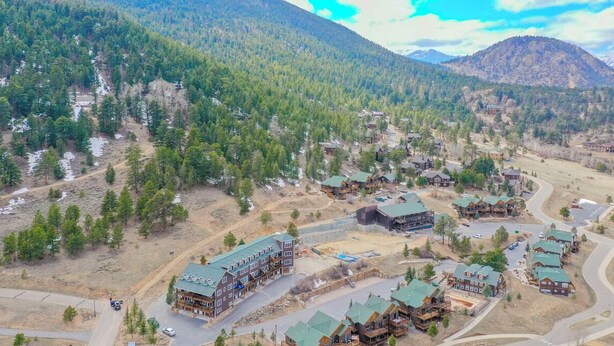 A lodge with multiple buildings, surrounded by forested mountains and a winding road. - Elk Meadow Condo #6047 (Estes Park)