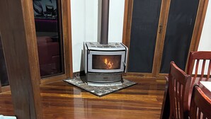 A room with a wood-burning stove, wooden flooring, a sofa, and a dining table with chairs. - Charming 3-bedroom cottage with AC in Torbanlea (Torbanlea)