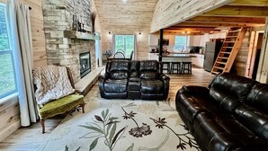Un interior de cabaña acogedor con chimenea de piedra, sofás de cuero, zona de comedor y cocina.