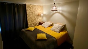 A single bed with a yellow and gray bedspread, two pillows, a nightstand with a lamp, and a textured wall. - EDEN gîte for 2 people with terrace and swimming pool in the heart of the Périgord Noir region (Doissat)