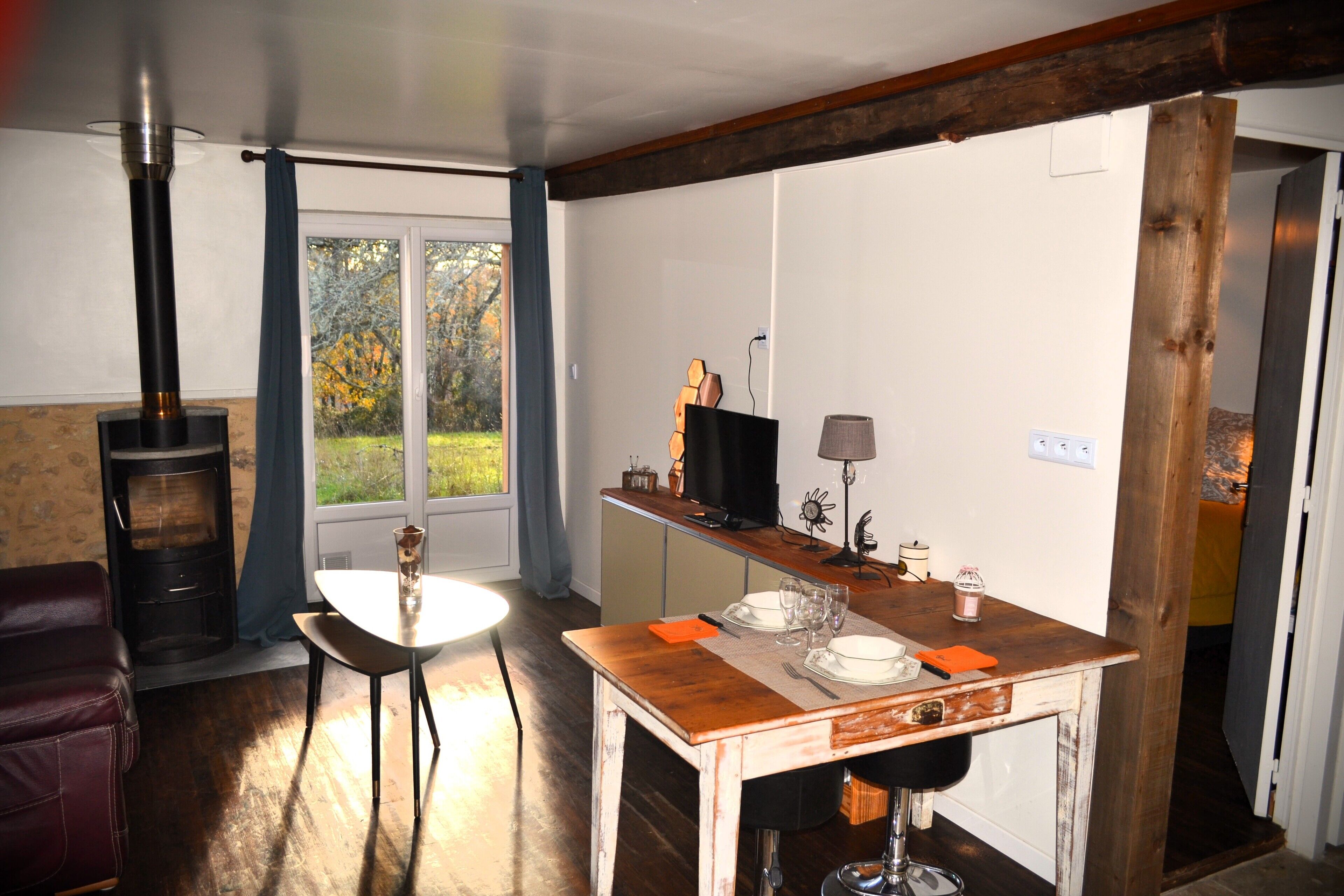 A cozy kitchen with a wood-burning stove, a dining table set for four, and a view of the outdoors through the window.