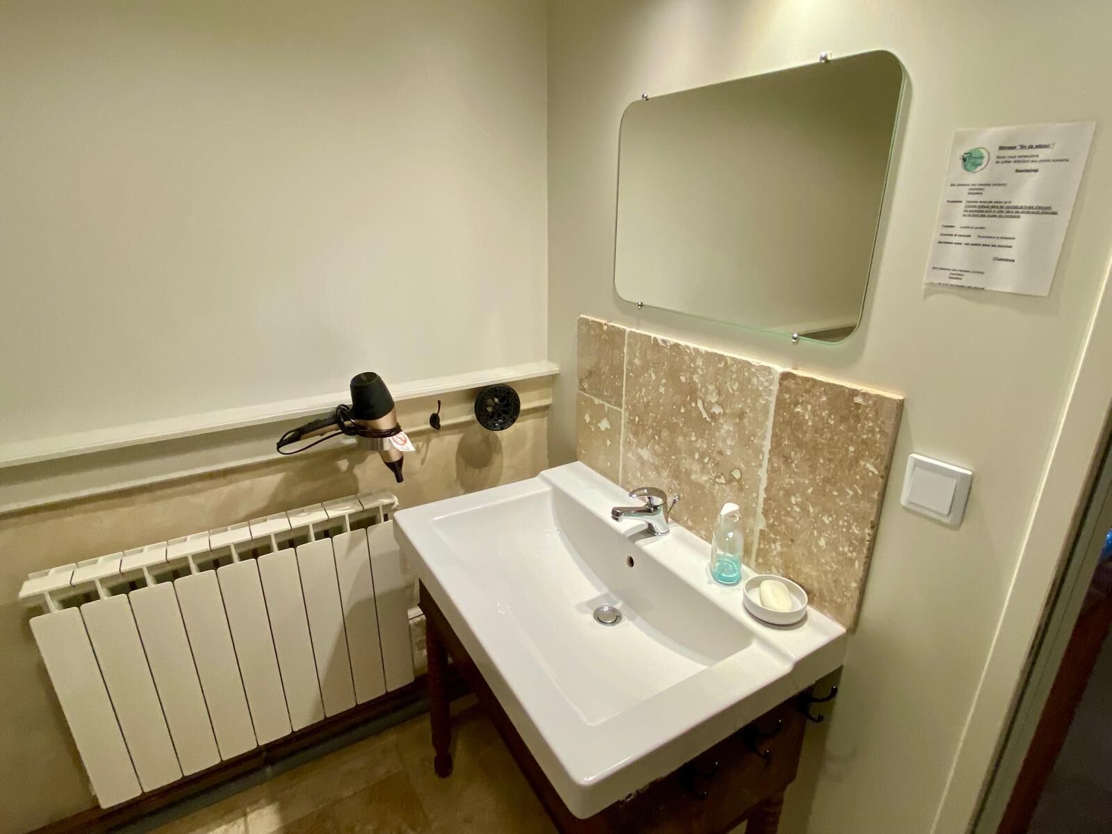 Une salle de bain avec un lavabo blanc, un miroir au-dessus, un porte-serviettes et un radiateur.