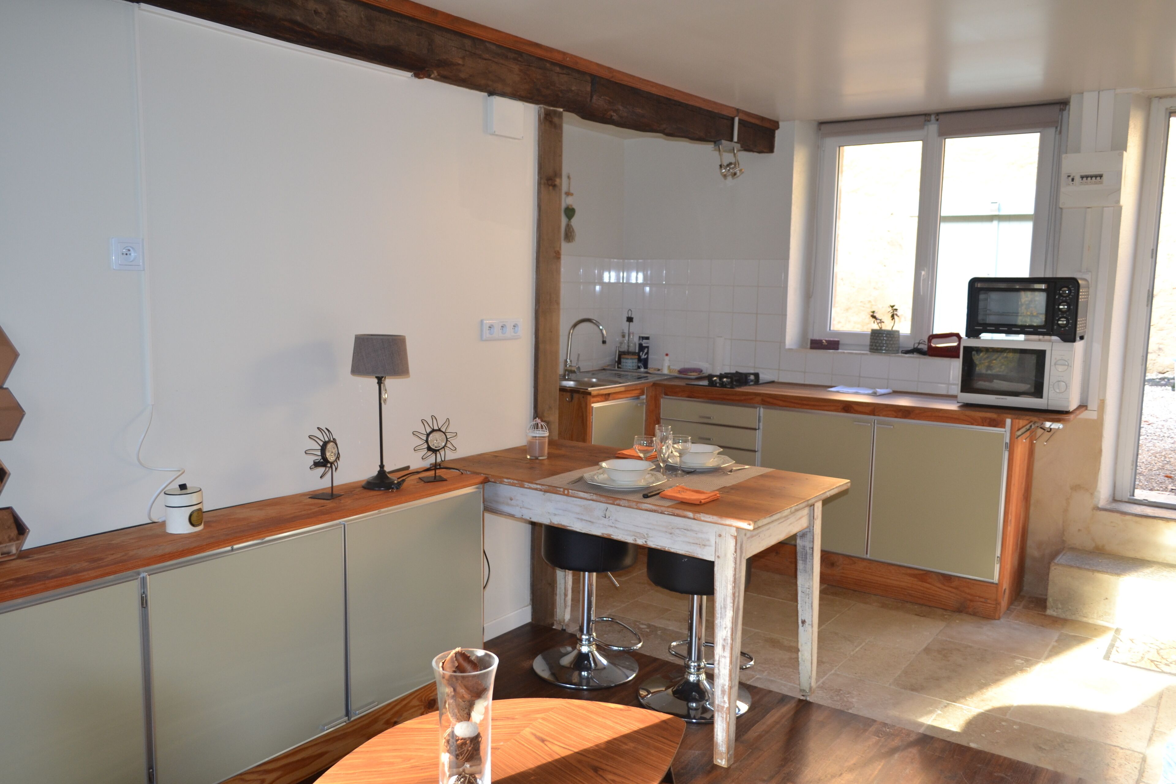 A kitchen with a wooden table, two bar stools, a microwave, and a window with a view.