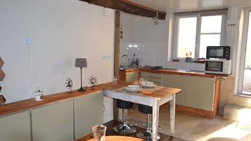 A kitchen with a wooden table, two bar stools, a microwave, and a window with a view.