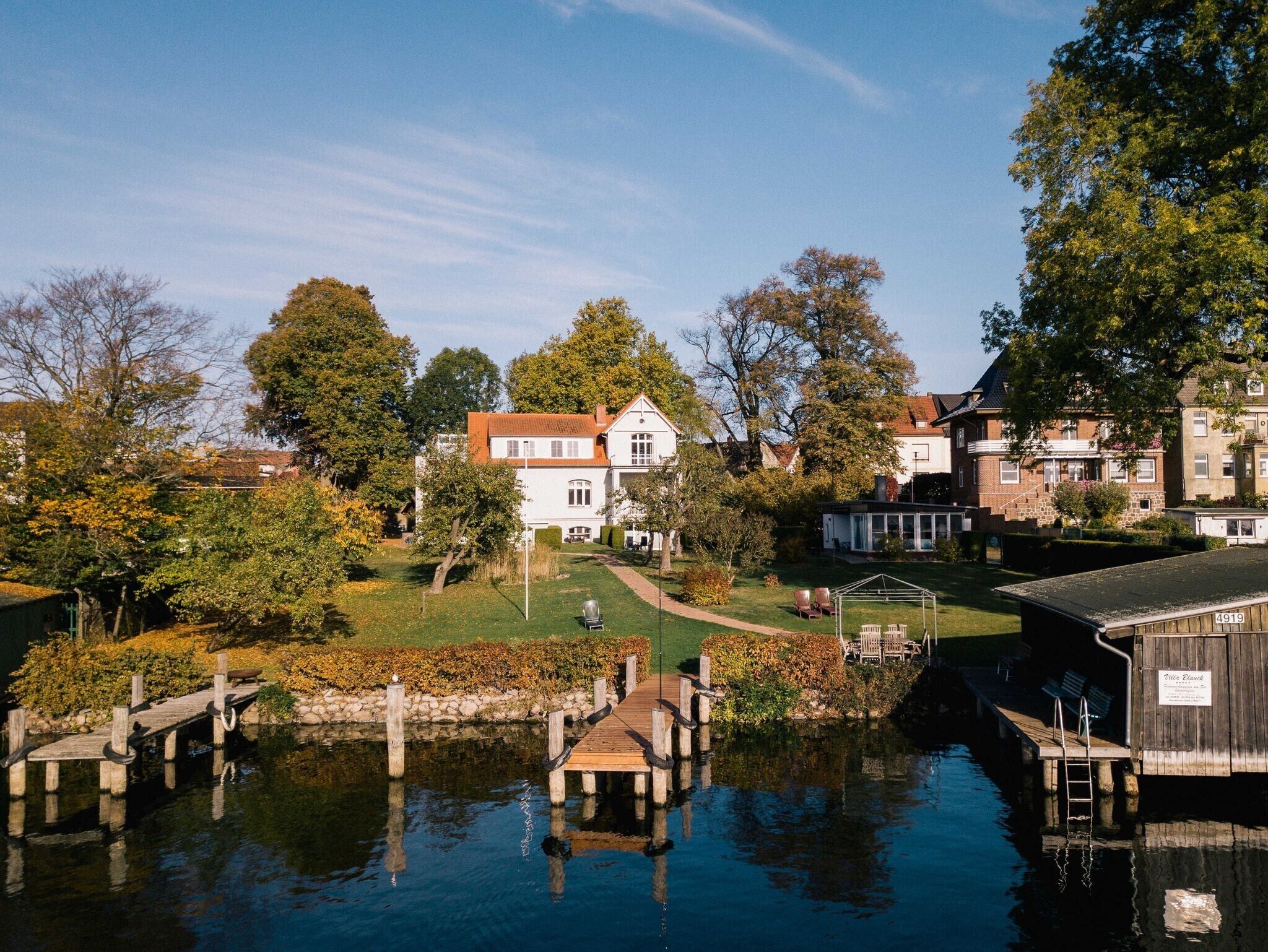 A waterfront property with a dock, a covered area, and a pathway leading to a white house.