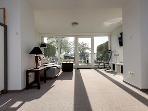 A modern living room with a sofa, coffee table, and a rocking chair. There is a television mounted on the wall and a large window providing a view of the outdoors. - Apartment 'Blanck 2' with Lake View, Private Terrace and Wi-Fi (Malchow)