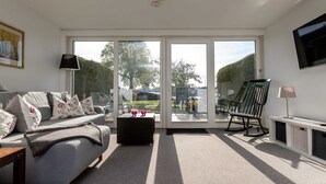 Ein modernes Wohnzimmer mit Sofa, Couchtisch, Fernseher und einer Schiebetür zu einem Außenbereich.