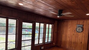 Una habitación con paredes de madera, ventanas amplias, un ventilador de techo y un dardo.