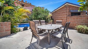 An outdoor patio with a round table and chairs, surrounded by a brick wall and greenery. - Medano Beach, Marina, Downtown, Walkable, Cozy (Cabo San Lucas)