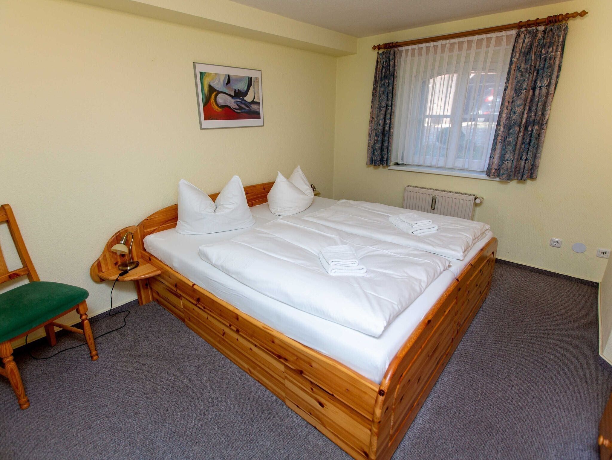A room with a wooden bed, a chair, a radiator, and a window with curtains.