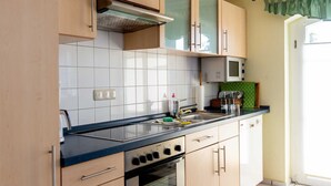A kitchen with light wood cabinets, a black countertop, a stove, and a microwave.