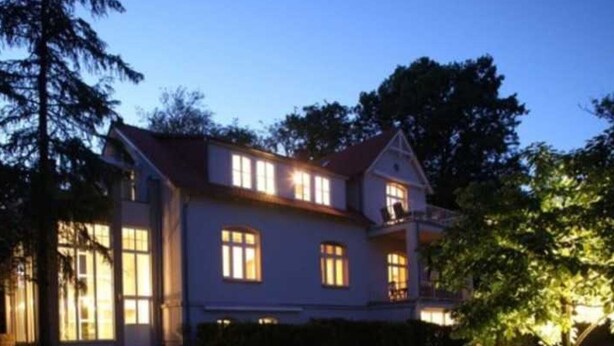 A two-story house with a red roof, multiple windows, and a well-maintained lawn.