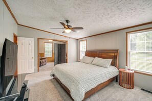 Une chambre avec un grand lit, un ventilateur de plafond, une télévision et une fenêtre avec des stores.