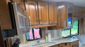 Une cuisine compacte pour camping-car, dotée de meubles en bois, d’un évier et d’une fenêtre offrant une vue sur la verdure.