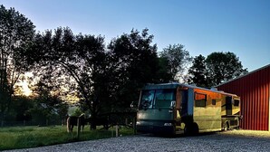 Une allée de gravier mène à un grand camping-car garé devant un bâtiment rouge.