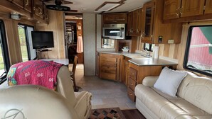 Un intérieur de camping-car compact comprenant un coin cuisine, un canapé, un téléviseur et un lit.