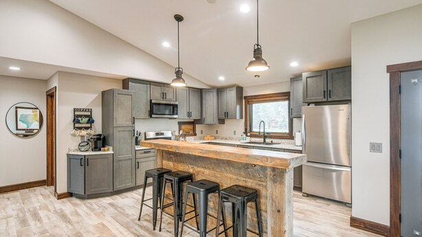 A modern kitchen with grey cabinets, a wooden island with stools, stainless steel appliances, and pendant lighting. - Pinedale Getaway Near Hiking, Skiing & Lakes! (Pinedale)