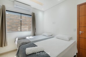 Ein Schlafzimmer mit zwei Betten, einem Fenster mit Vorhängen, einem Holzschrank und einer Klimaanlage.