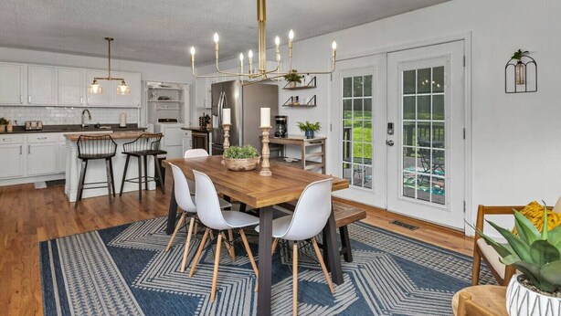 Een moderne keuken met witte kasten, een houten eettafel en een kroonluchter.