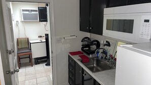 Een compact keukenblok met een magnetron, gootsteen en een klein eethoekje met een stoel en tafel.