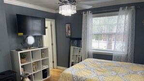 Een slaapkamer met een bed, een televisie, een boekenkast en een raam met gordijnen.