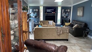 Een woonkamer met een beige bank, een bruine leren bank en een aan de muur bevestigde televisie.