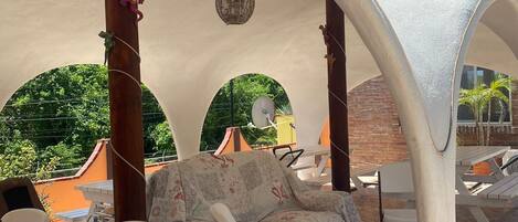 Un espace extérieur aménagé en terrasse, avec un coin salon abrité, des tables et des chaises.