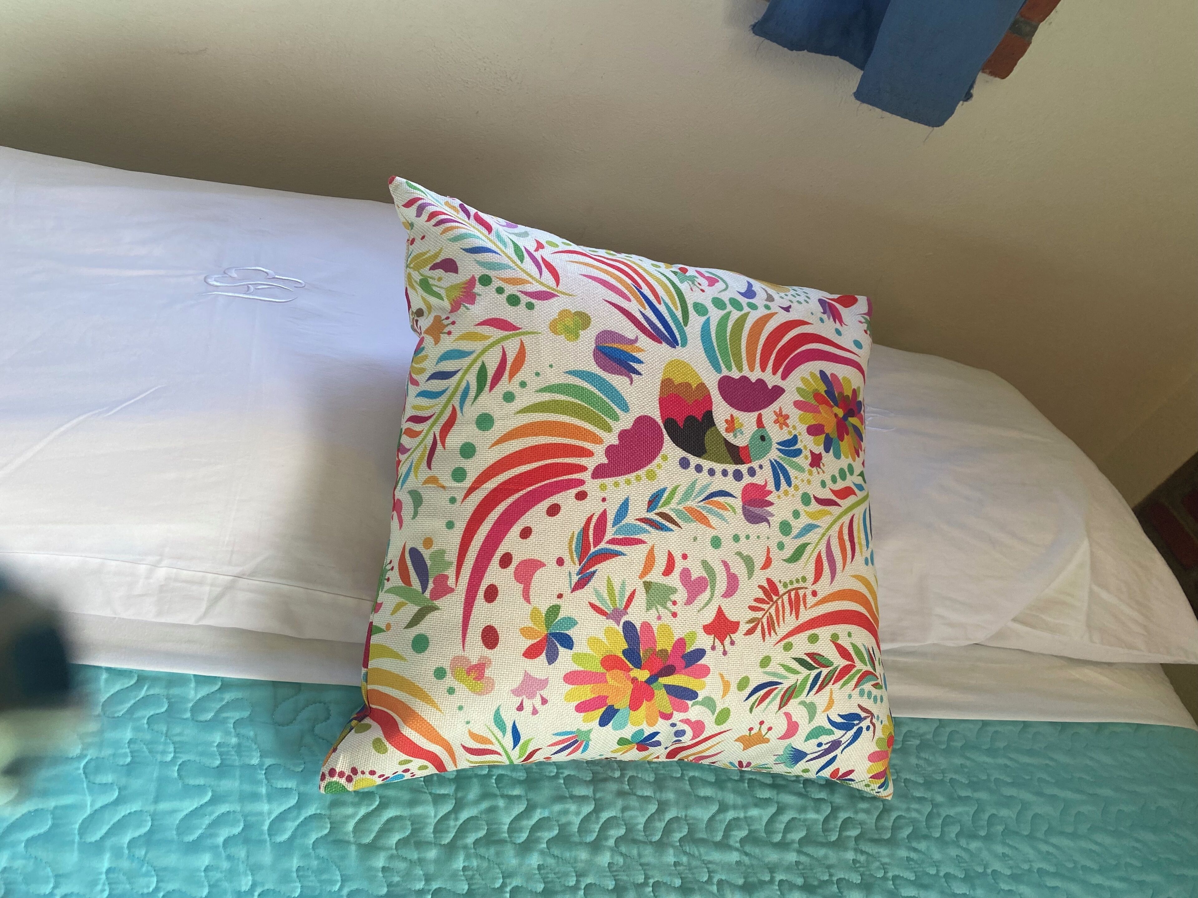 A bed with a colorful floral pillow and a teal quilted bedspread.