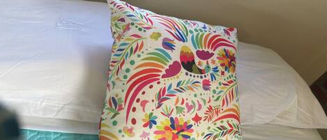 A bed with a colorful floral pillow and a teal quilted bedspread.