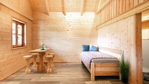 Ein Holzhütten-Interieur mit einem Bett, einem kleinen Tisch mit Hocker und einem Fenster.