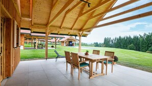 Eine hölzerne Veranda mit Tisch und Stühlen, ein Pool im Hintergrund und Blick auf eine grüne Landschaft.