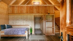 Ein gemütliches Schlafzimmer in einer Holzhütte mit Bett, einer kleinen Pflanze und einer Treppe zu einem Erkerraum.