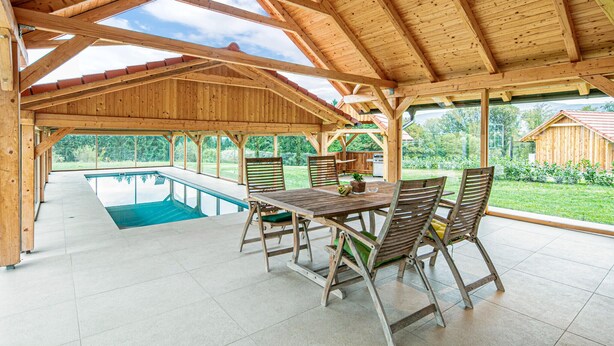 Eine hölzerne Veranda mit Pool, Sitzgelegenheiten im Freien und Blick auf die umliegende Landschaft.