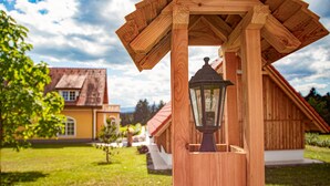 Ein hölzerner Pavillon mit einer Laterne in der Mitte, umgeben von einem gepflegten Rasen und einem Haus mit rotem Dach im Hintergrund.
