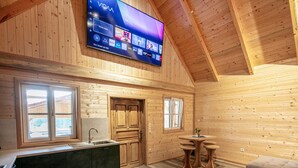 Ein Holzblockhaus-Innenraum mit Fernseher, der verschiedene Streaming-Dienste anzeigt, einer Küchenzeile und einem Essbereich.
