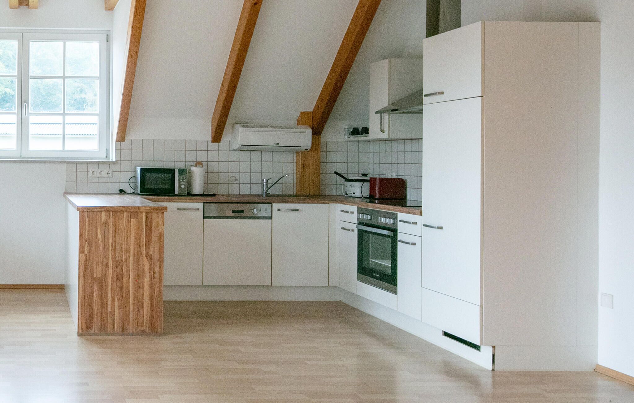 Een moderne keuken met witte kasten, een houten aanrecht, een ingebouwde magnetron, een vaatwasser en een oven.