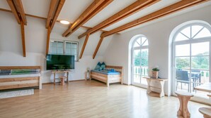 A spacious room with wooden beams, a bed, a TV, and large windows.