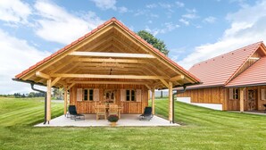 Eine Holzhütte mit überdachter Terrasse, einem Essbereich und einem Gebäude mit rotem Dach im Hintergrund.