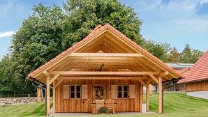 Eine Holzhütte mit Satteldach, einer Veranda und einem Pool davor.