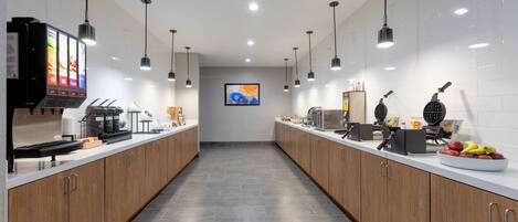 A modern kitchen with wooden cabinets, a coffee machine, waffle maker, and a fruit bowl.